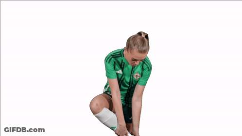 Woman In Green Adidas Shirt Holding Shoe To Ear GIF