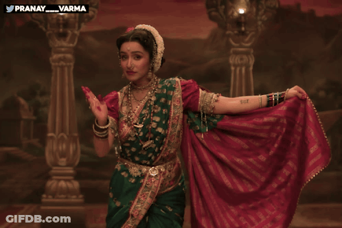 Woman In Green And Red Dress Dancing In Front Of Pranay Varma Painting GIF