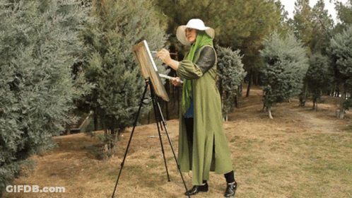 Woman In Green Coat Painting On Easel In Woods GIF