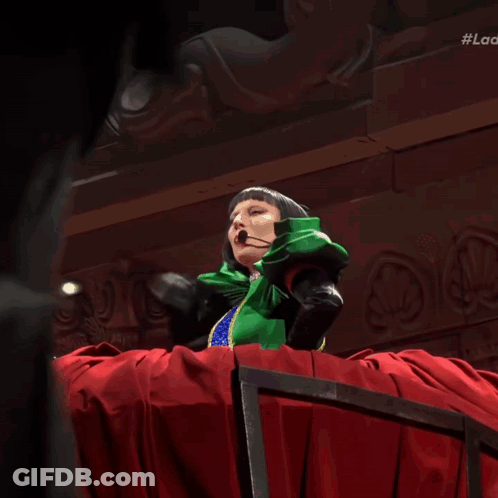 Woman In Green Dress And Black Gloves In Front Of Red Spiked Curtain GIF