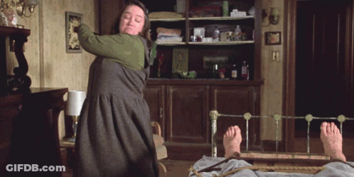 Woman In Green Dress Holding Stick Over Man On Bed GIF