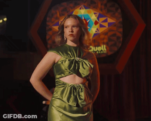 Woman In Green Dress Holding Sticks In Front Of Stained Glass Saying Hell GIF