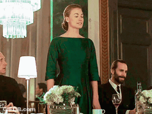 Woman In Green Dress Standing Before Group At Table GIF