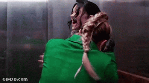 Woman In Green Shirt Hugging Another Woman In Dark Room GIF