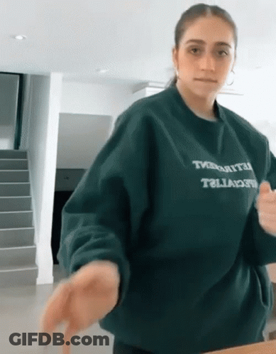 Woman In Green Sweater Saying Tivoli Standing In Front Of Stairs GIF