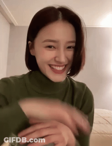 Woman In Green Turtleneck Smiling And Waving GIF