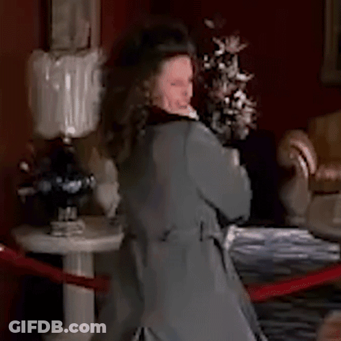 Woman In Grey Coat Standing By Flowers GIF