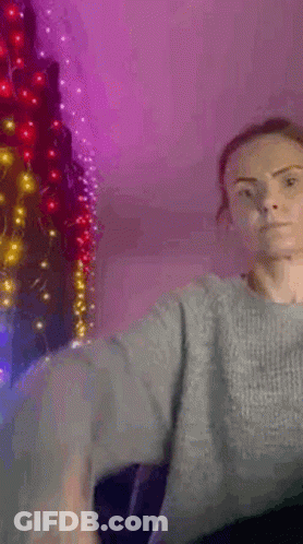 Woman In Grey Sweater By Christmas Tree With Lights GIF