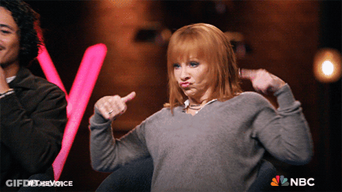 Woman In Grey Sweater Making Funny Face In Front Of NBC Sign GIF