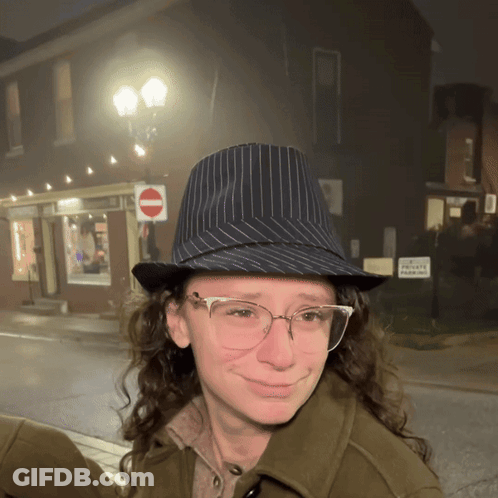 Woman In Hat And Glasses Smiling In Front Of No Parking Sign GIF