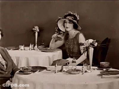 Woman In Hat Sitting At Table With Plates And Cups GIF
