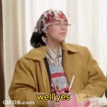 Woman In Head Scarf And Glasses Sitting With Drink And Straw GIF