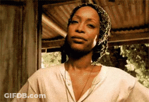 Woman In Head Scarf And White Shirt In Front Of Wooden Building GIF