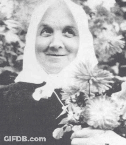 Woman In Head Scarf Holding Flowers And Smiling GIF
