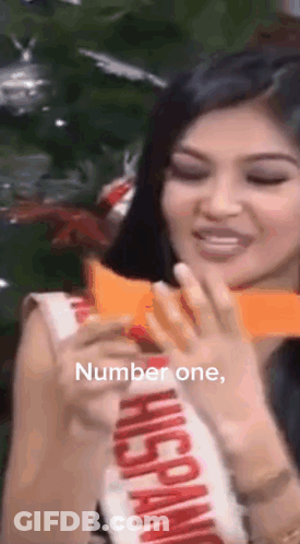 Woman In Hispanic Sash Holding Paper In Front Of Christmas Tree GIF