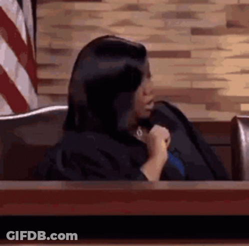 Woman In Judge Robe Sitting At Table In Front Of American Flag GIF