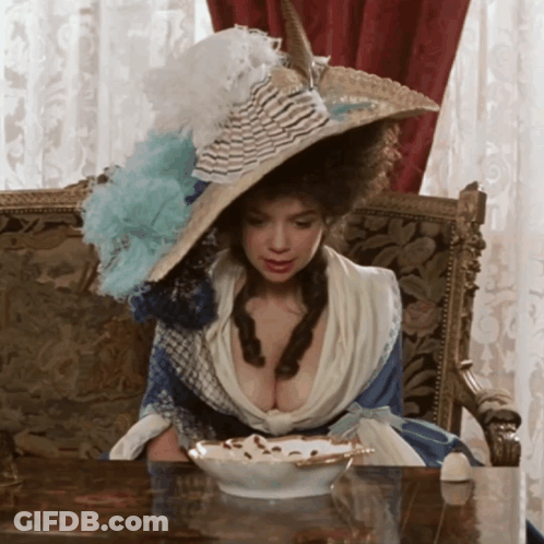 Woman In Large Hat Sitting At Table With Bowl Of Food GIF