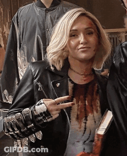 Woman In Leather Jacket Giving Peace Sign Holding Book GIF