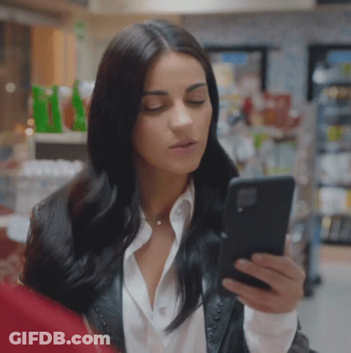 Woman In Leather Jacket Looking At Phone In Store GIF