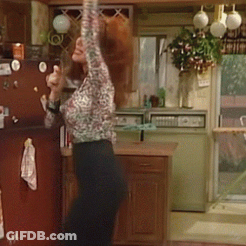 Woman In Leopard Shirt Arms Up In Kitchen GIF