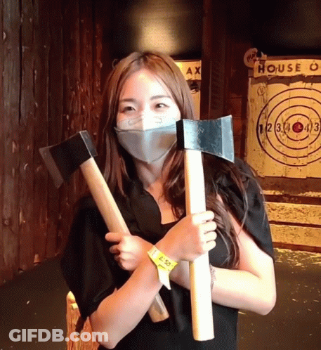 Woman In Mask Holding Two Axes With House Target GIF
