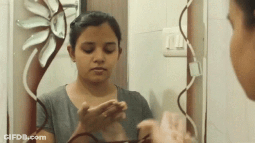 Woman In Mirror Rubbing Lotion On Face GIF