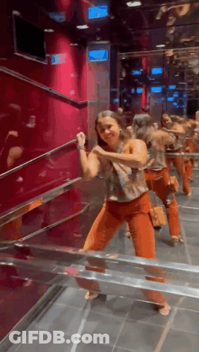 Woman In Orange Pants Dancing In Front Of Exit Sign GIF