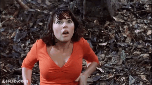 Woman In Orange Shirt Standing In Woods GIF