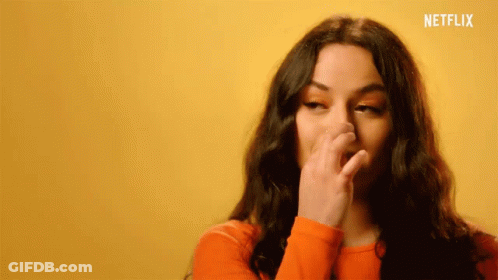 Woman In Orange Sweater Covering Nose GIF