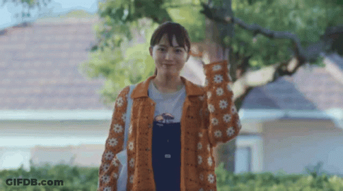 Woman In Overalls And Orange Jacket With Flowers GIF