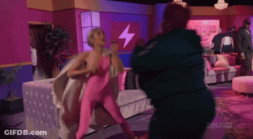 Woman In Pink Bodysuit Fighting Man In Green Jacket In Front Of Zeusz Sign GIF