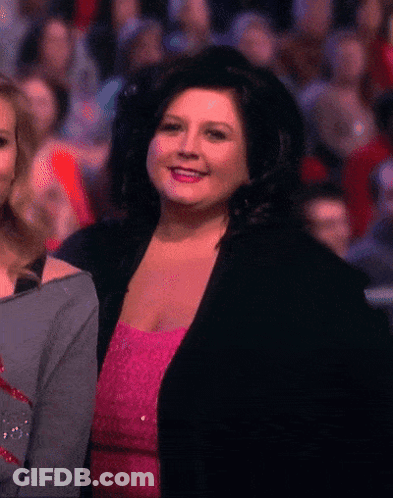 Woman In Pink Dress And Black Jacket Smiling Before Crowd GIF