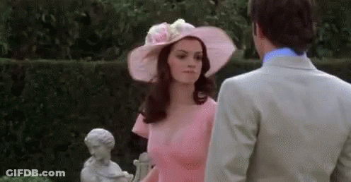 Woman In Pink Dress And Hat Next To Man In Suit GIF