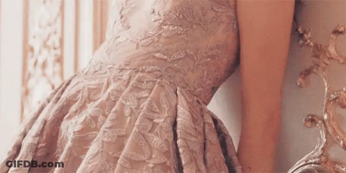 Woman In Pink Dress Leaning Against Wall Looking In Mirror GIF