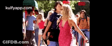 Woman In Pink Dress Next To Man In Blue Shirt In Front Of Crowd GIF