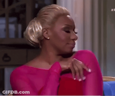 Woman In Pink Dress Sitting On Couch With Hand On Chest GIF