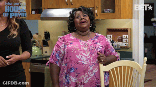 Woman In Pink Floral Shirt Sitting In Kitchen With House Of Payne Logo GIF