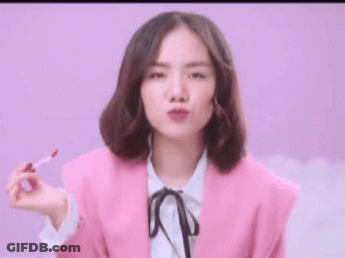 Woman In Pink Jacket Holding Lip Gloss GIF