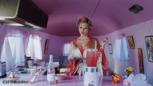 Woman In Pink Jacket Sitting At Table In Front Of Yellow Wall GIF