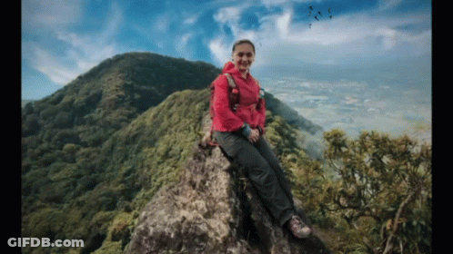 Woman In Pink Jacket Sitting On Rocky Mountain GIF