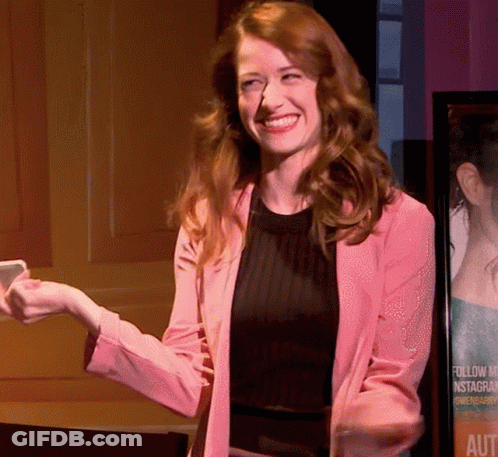 Woman In Pink Jacket Smiling In Front Of Follow Us Instagram Poster GIF