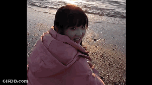 Woman In Pink Jacket Standing On Beach GIF