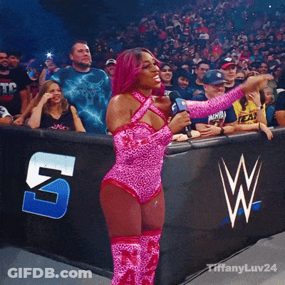 Woman In Pink Leopard Print Holding Microphone In Front Of Crowd With W Logo GIF