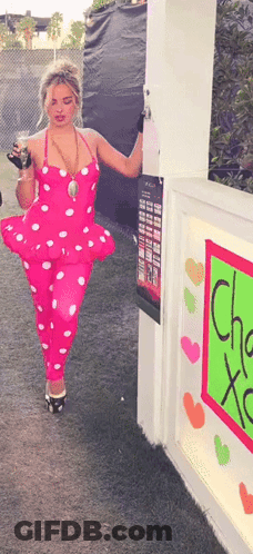 Woman In Pink Polka Dot Outfit Standing In Front Of Cha Xoxo Sign GIF