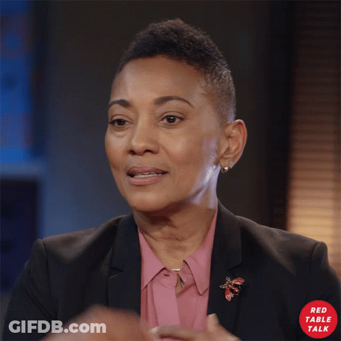 Woman In Pink Shirt And Black Jacket With Red Table Talk Logo GIF