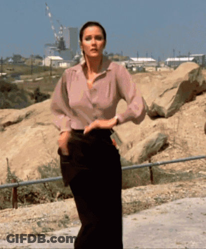 Woman In Pink Shirt And Black Pants Standing In Front Of Building GIF