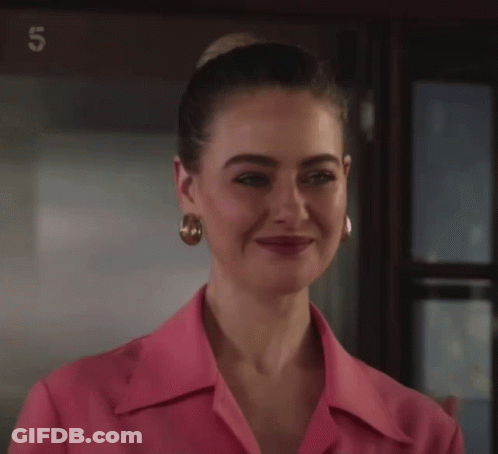 Woman In Pink Shirt And Gold Earrings Smiling In Front Of Sign Saying 5 GIF
