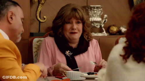 Woman In Pink Shirt And Scarf Eating At Table GIF