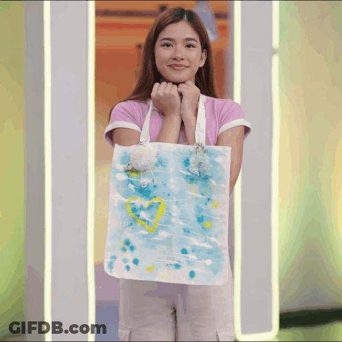 Woman In Pink Shirt Holding Blue And White Tote Bag With Yellow Heart GIF