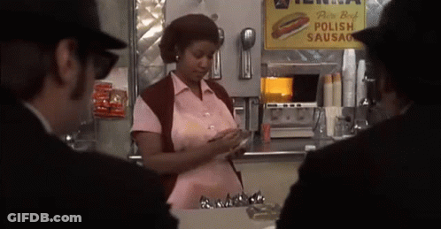 Woman In Pink Shirt In Front Of Polish Sausage Sign GIF
